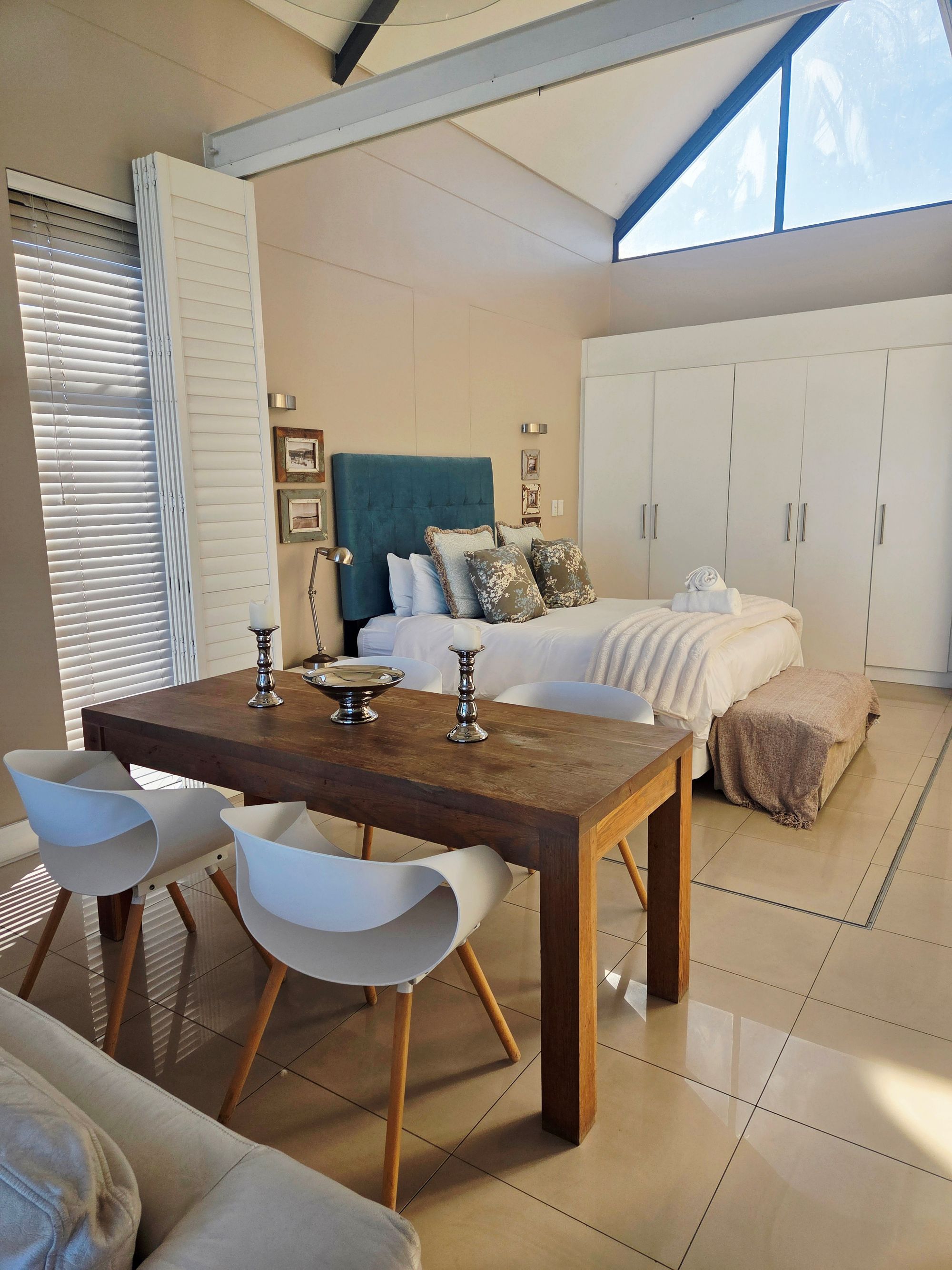 A modern bedroom with a large bed, a dining table with chairs, and a wardrobe.