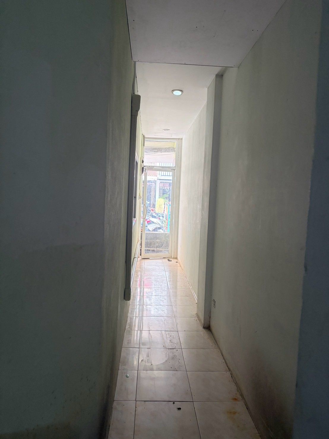 Un pasillo estrecho con piso de baldosas que conduce a una puerta con panel de vidrio.