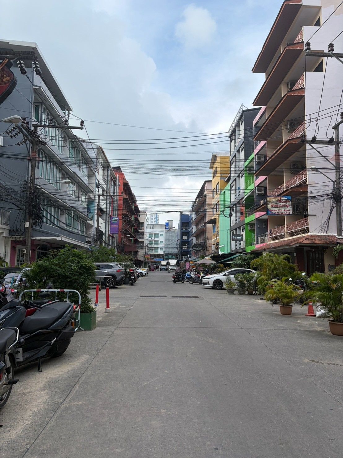 A street lined with multi-story buildings, some with balconies, and parked vehicles on the side.