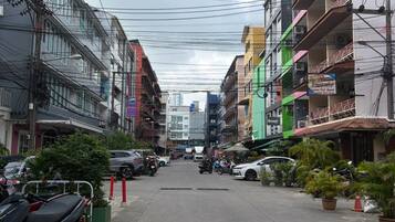 A street lined with multi-story buildings, some with balconies, and parked vehicles on the side.