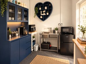 Una cocina compacta con repisa en forma de corazón, cafetera, microondas y refrigerador.
