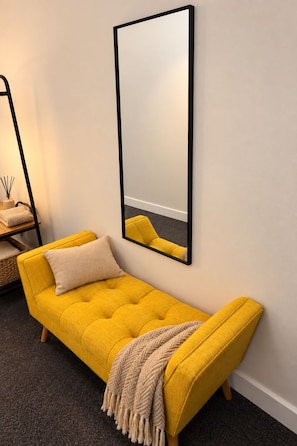 Un sofá amarillo con una manta, un espejo en la pared y una mesita con velas.