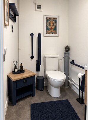 Un baño moderno con inodoro, bidé y un pequeño tocador de madera con un cesto de basura.