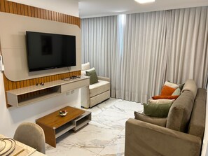 En moderne stue med et fladskærms TV ophængt på væggen, en sofa, et sofabord og et spiseområde med stole.