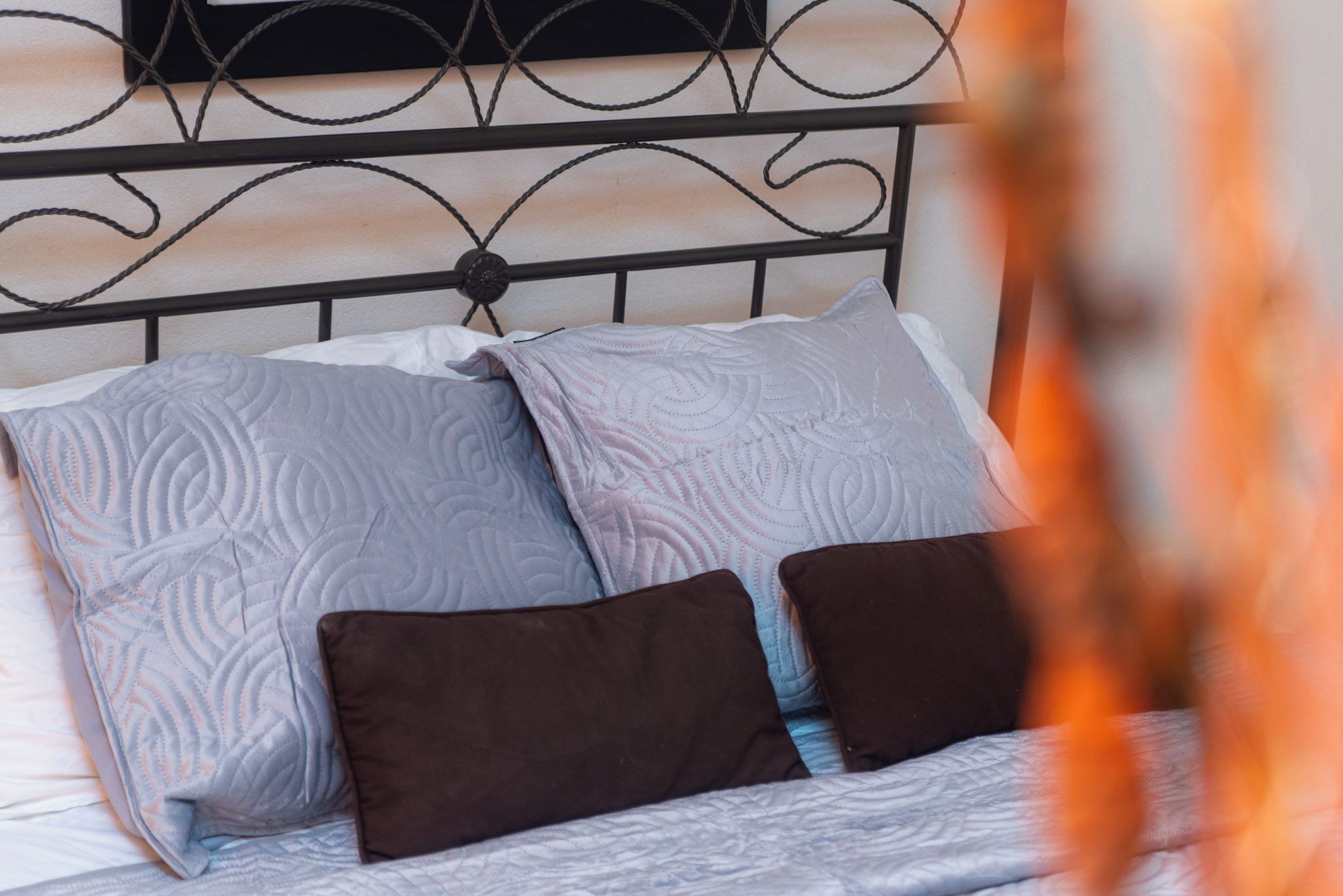 Un lit avec une tête de lit en métal, deux oreillers et une couvre-lit à motifs.