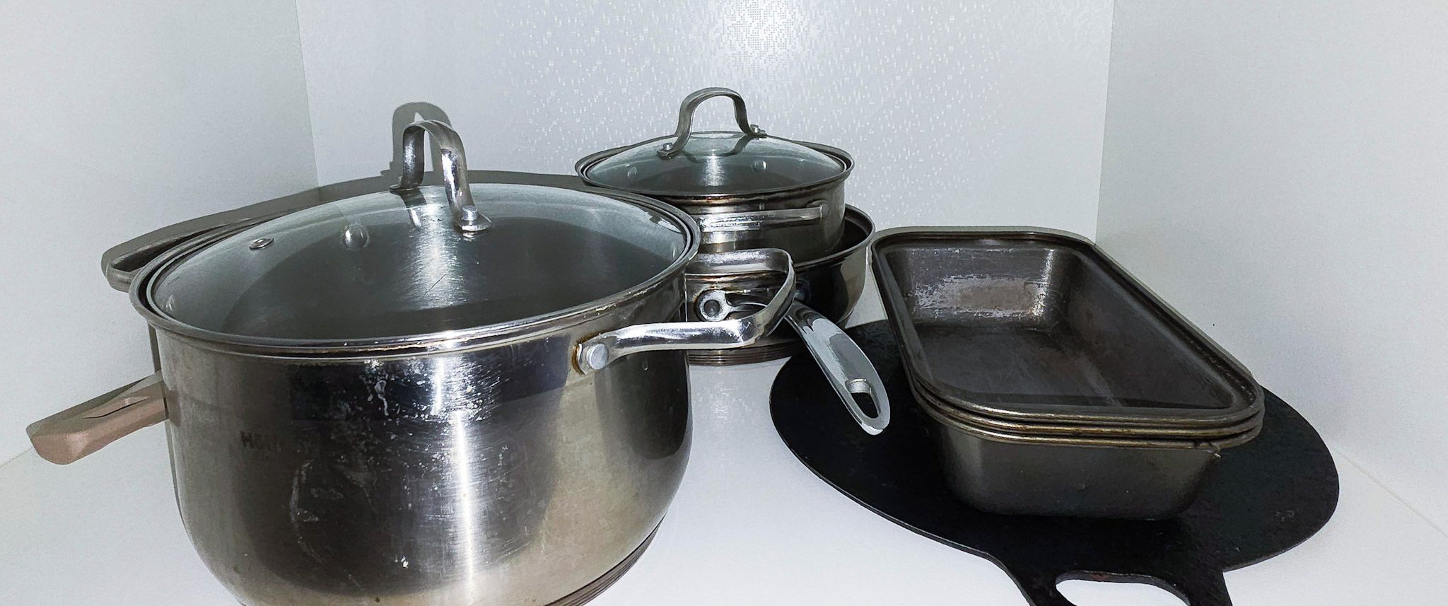 Een roestvrijstalen pan met deksel, een kleinere pan met deksel, en een rechthoekige braadpan.