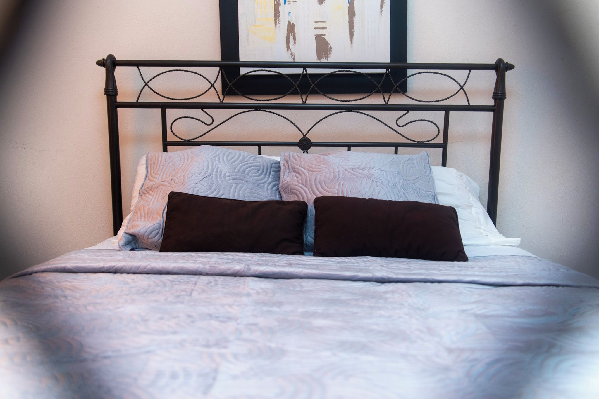 A bed with a metal headboard, two pillows, and a patterned bedspread.