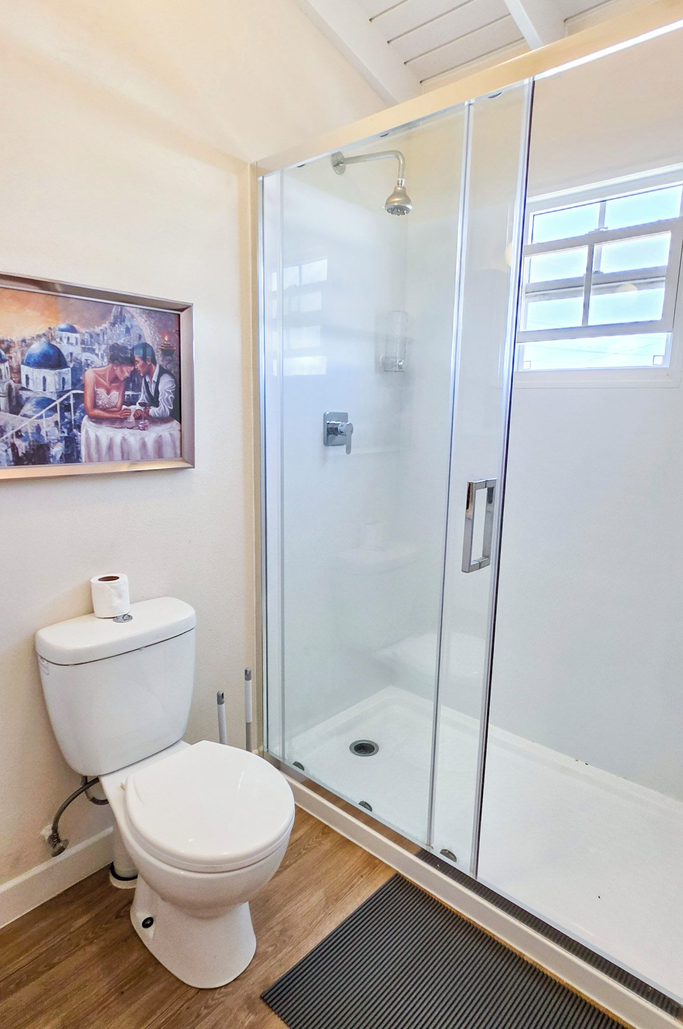 A modern bathroom with a glass-enclosed shower, a toilet, and a framed painting on the wall.