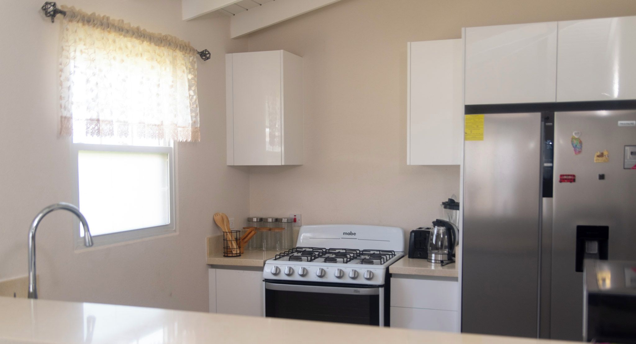 Une cuisine de taille réduite, équipée d’une cuisinière à gaz, d’un réfrigérateur et d’une fenêtre avec un rideau.