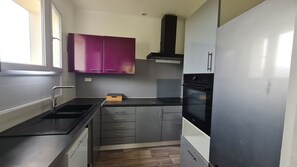 Une cuisine de taille réduite avec des meubles gris, une cuisinière noire et un réfrigérateur blanc.