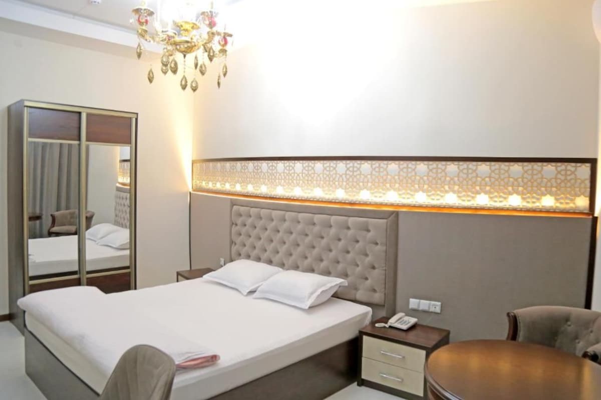 A hotel room with a bed, bedside table, chair, wardrobe, and a decorative wall panel.