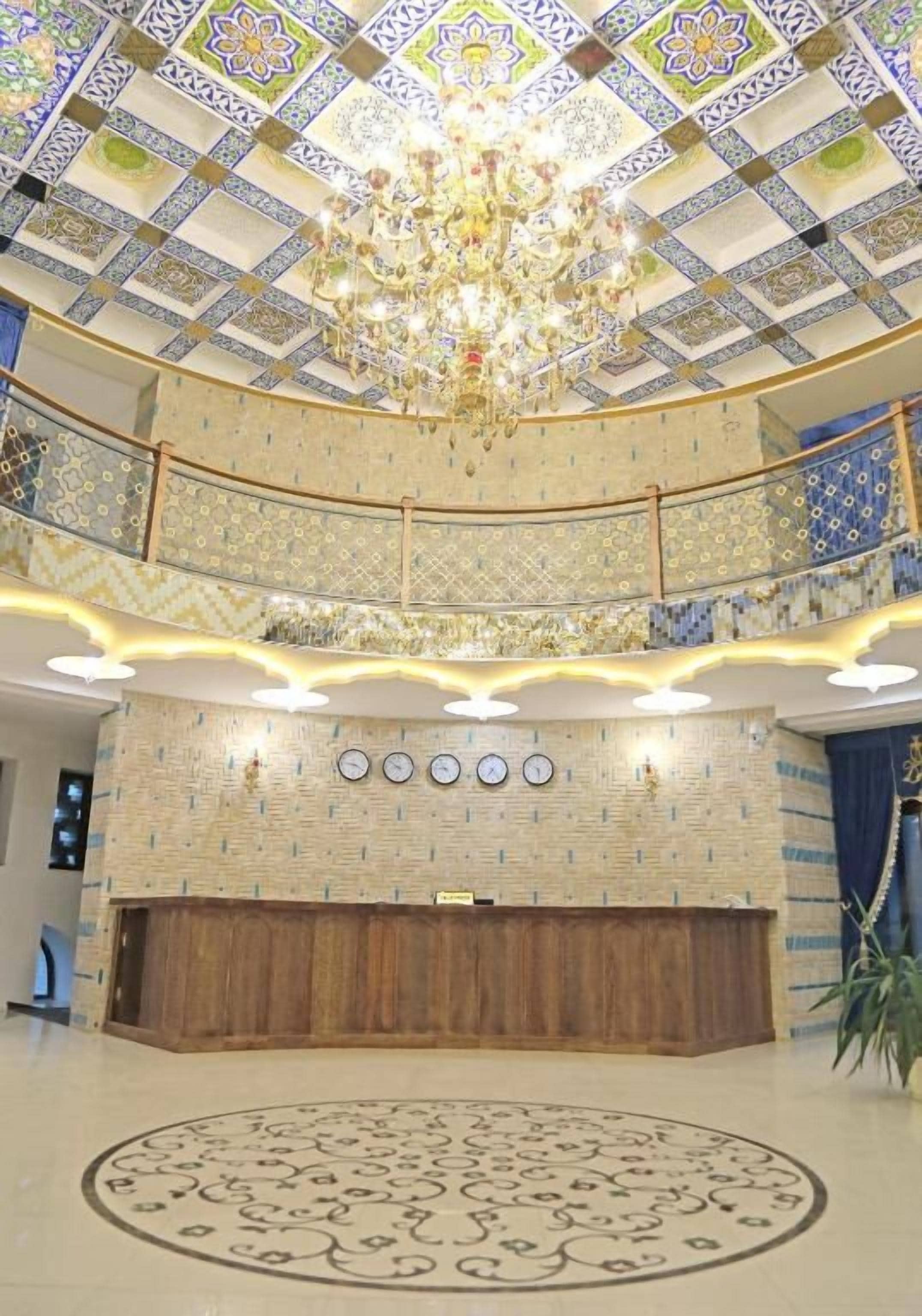 A lobby with a grand chandelier, a reception desk, and a patterned floor.