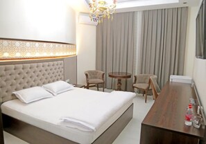 A hotel room with a large bed, two armchairs, a small round table, and a wooden desk. - Grand Ark Bukhara (Bukhara)