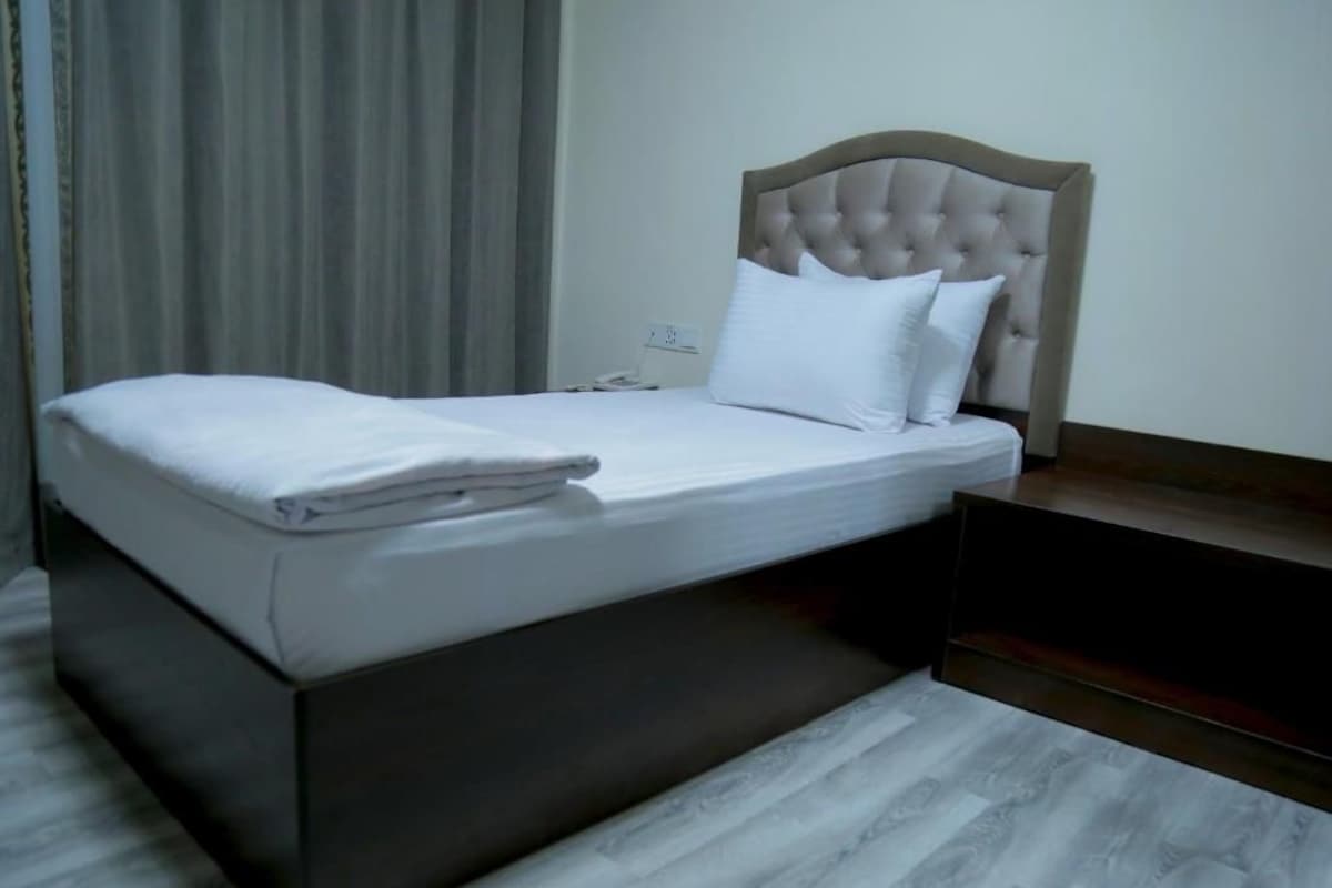 A neatly made bed with a headboard, a bedside table, and a power outlet on the wall.