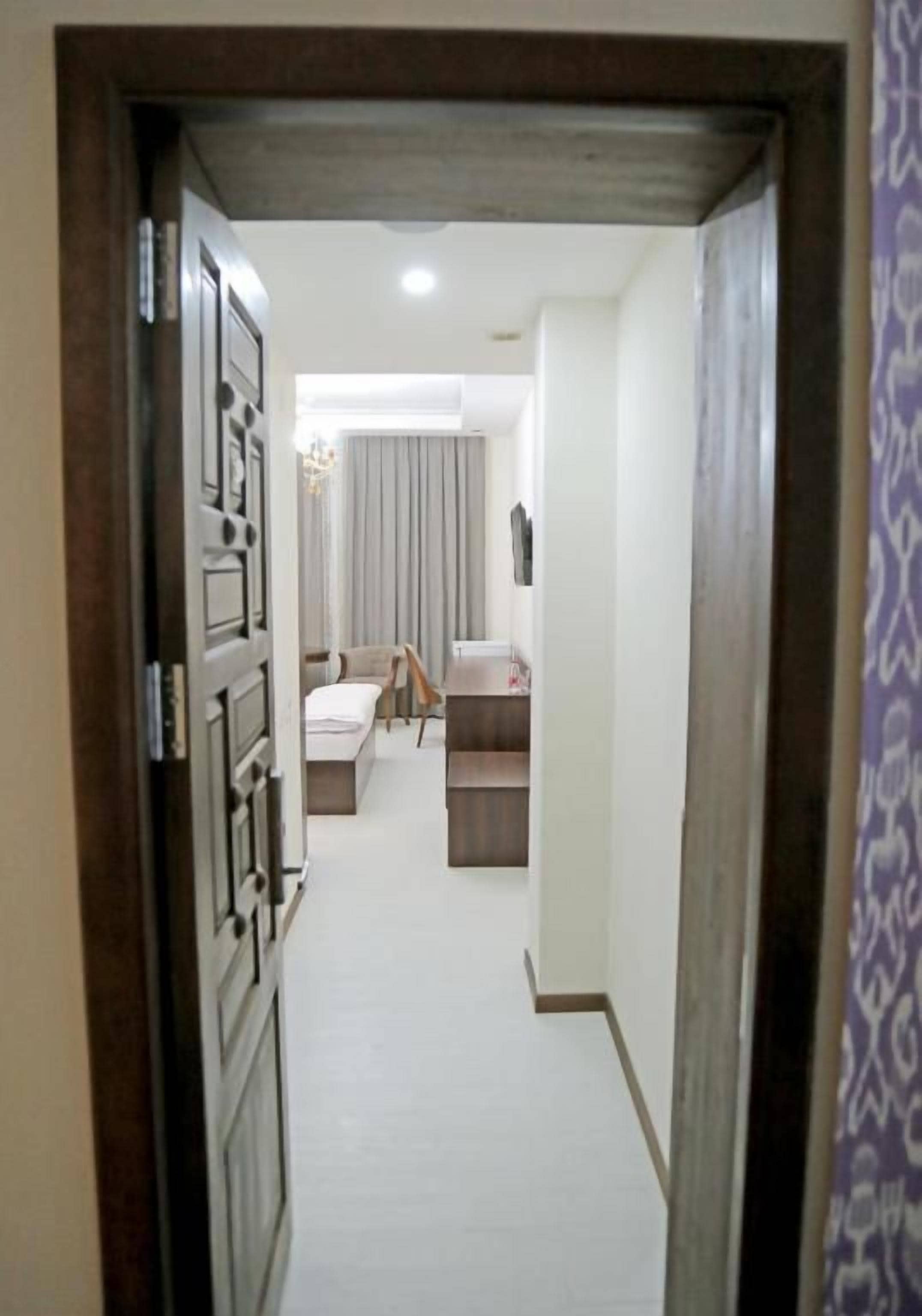 A hallway leading to a bedroom with a bed, bedside table, and a dresser.