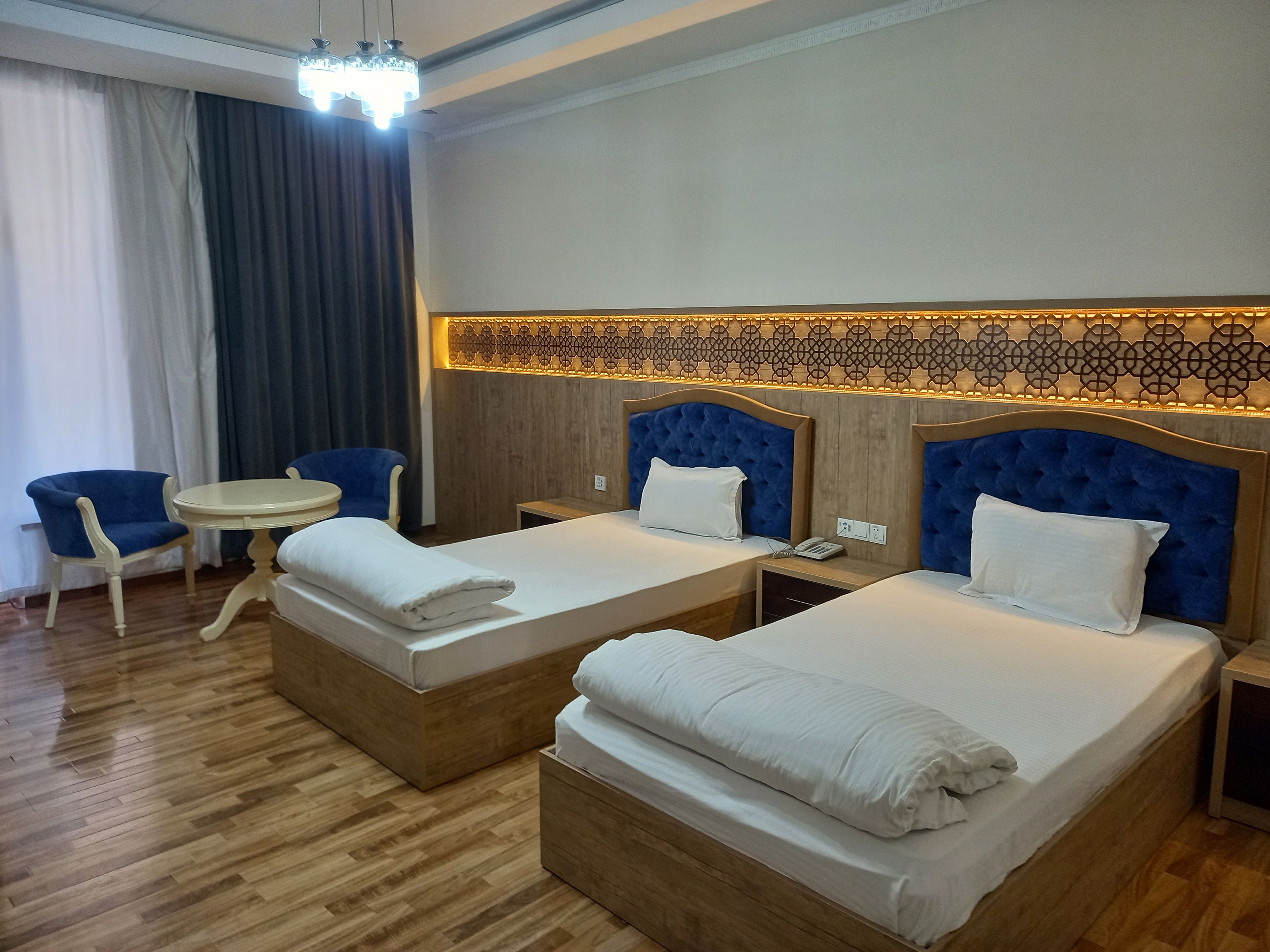 Habitación de hotel con dos camas, una mesita redonda pequeña, una silla y un panel decorativo en la pared.