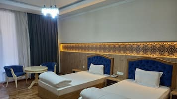 Habitación de hotel con dos camas, una mesita redonda pequeña, una silla y un panel decorativo en la pared.