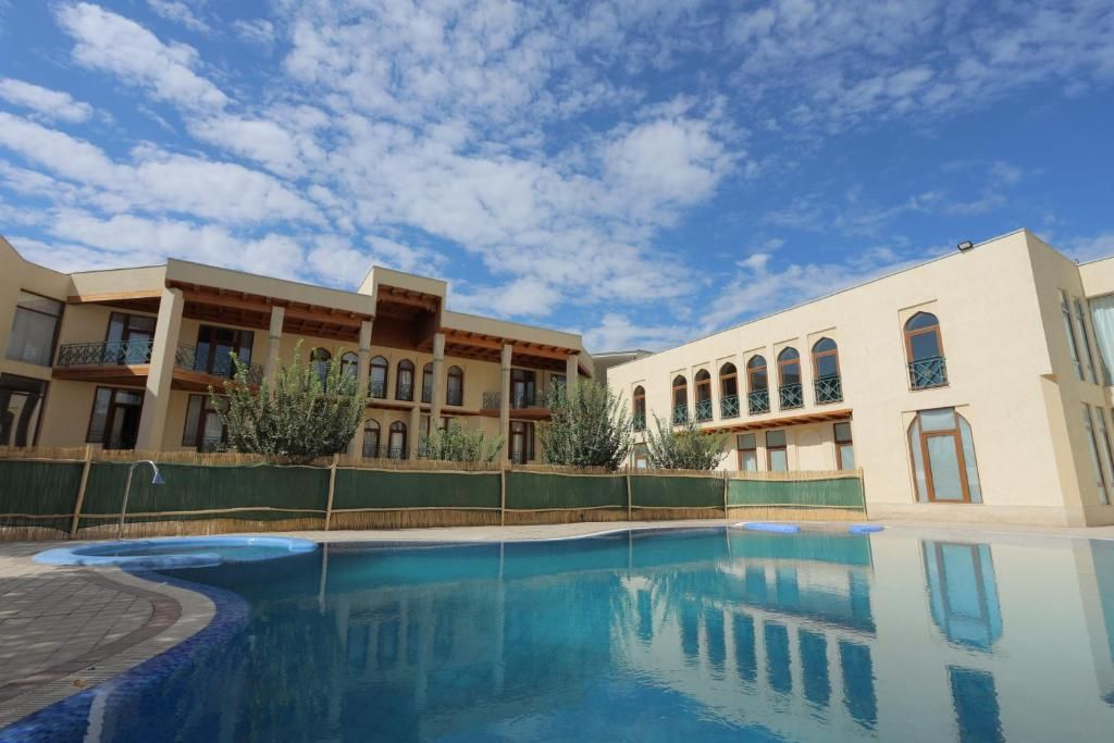 A hotel with a swimming pool, a covered patio, and a building with arched windows.