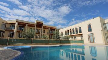 A hotel with a swimming pool, a covered patio, and a building with arched windows.