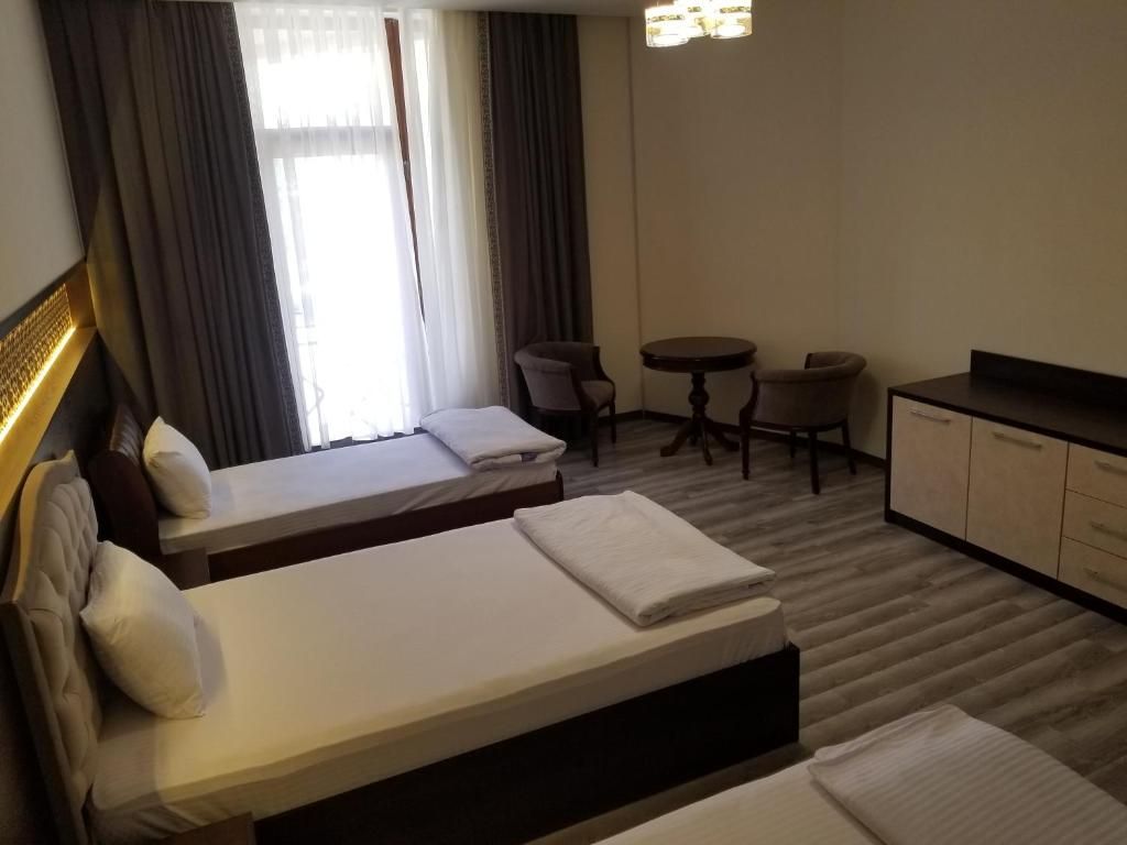 Habitación de hotel con dos camas, una mesita, dos sillas, un escritorio y un armario.