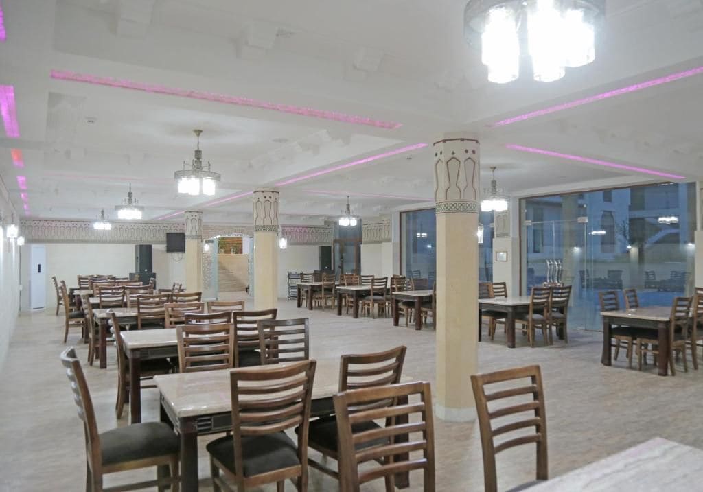 A spacious dining area with multiple tables and chairs, ceiling lights, and pillars.