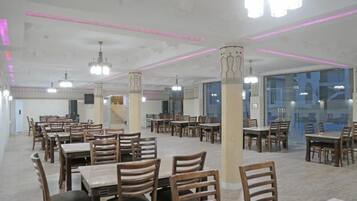A spacious dining area with multiple tables and chairs, ceiling lights, and pillars.