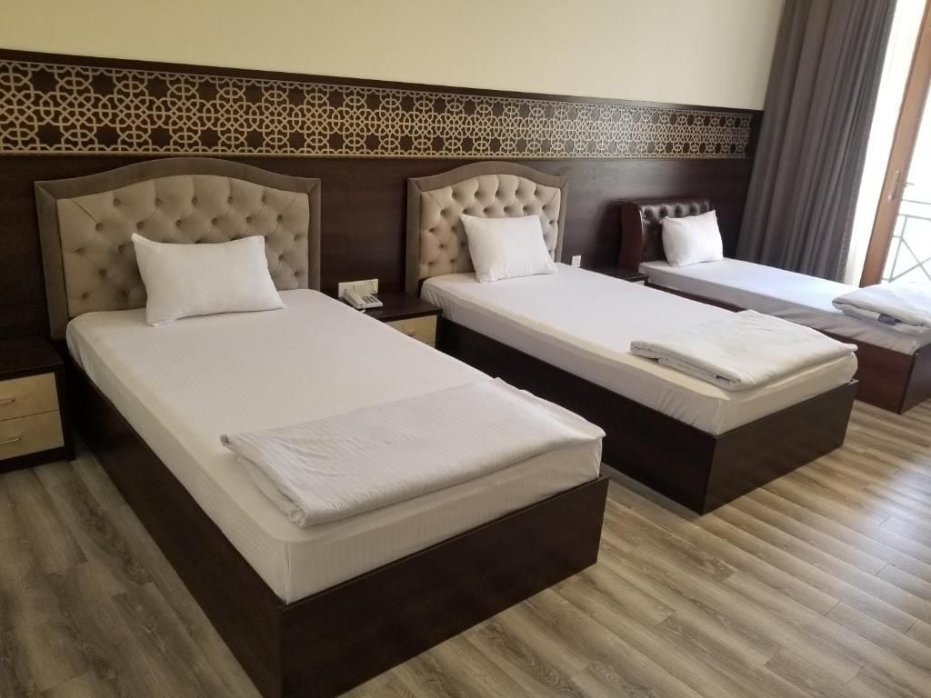 A hotel room with two beds, a nightstand, and a window with curtains.