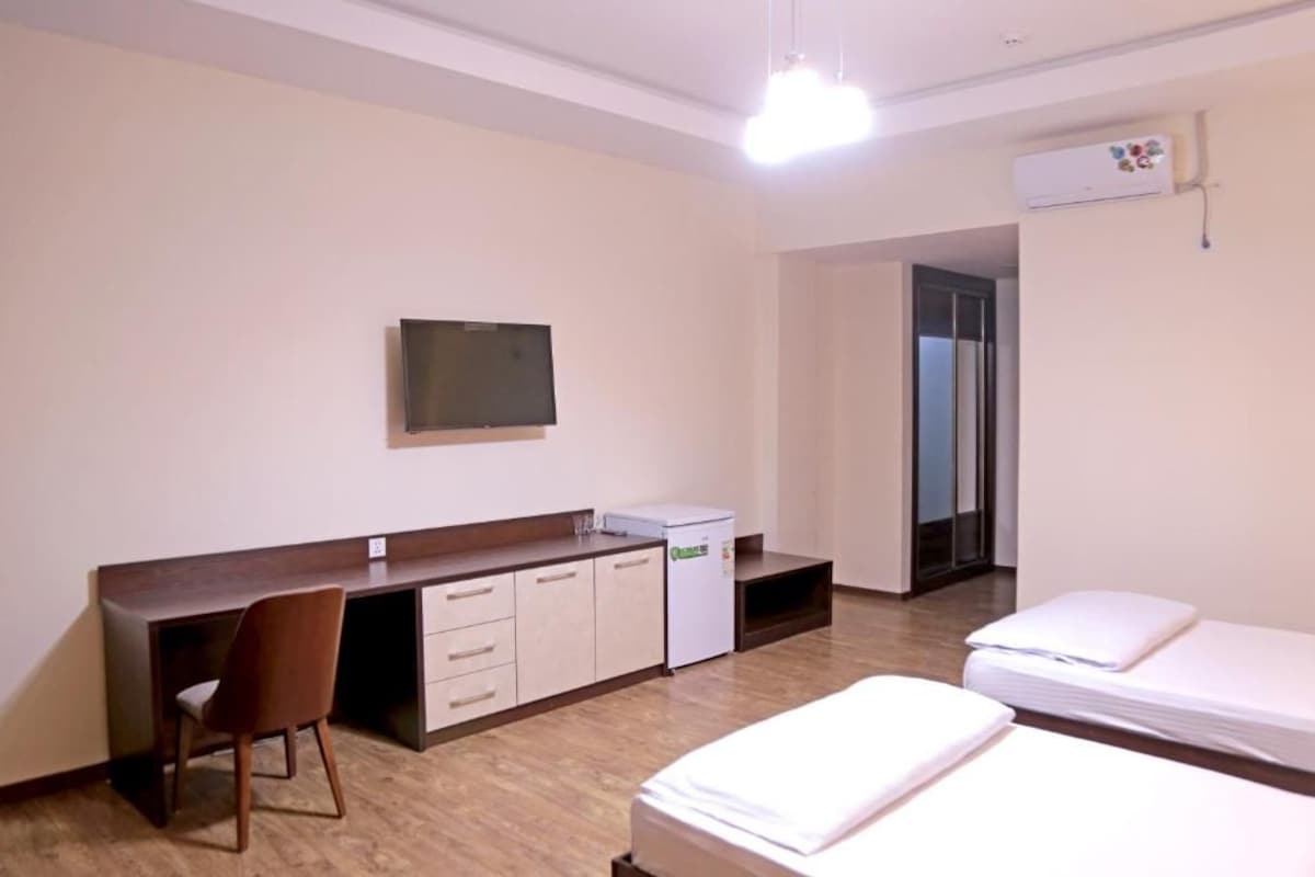 A hotel room with a bed, a desk, a chair, a television, and a small refrigerator.