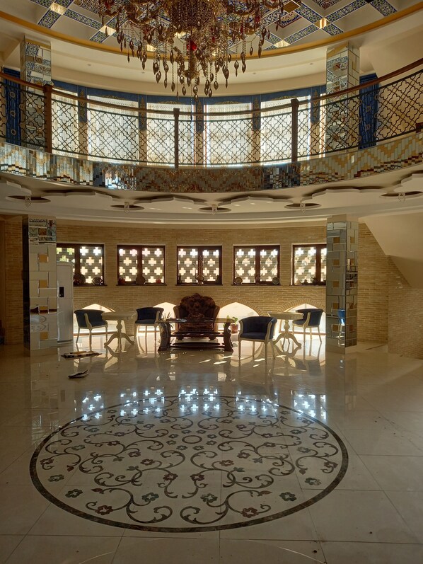 A spacious lobby with a central seating area, a chandelier, and a high ceiling with intricate patterns. - Grand Ark Bukhara (Bukhara)
