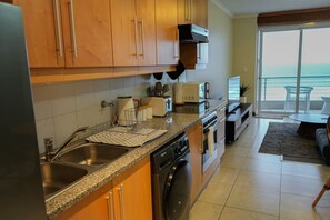 Una cucina moderna con elettrodomestici in acciaio inossidabile, lavastoviglie e un'ampia finestra con vista su un balcone che si affaccia sull'oceano.