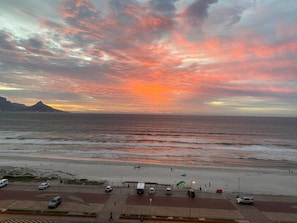 Vista de la playa con un atardecer, zona de estacionamiento y una montaña al fondo.