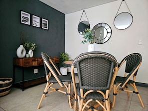 Un área de comedor con sillas de mimbre, una mesa redonda y relojes en la pared.