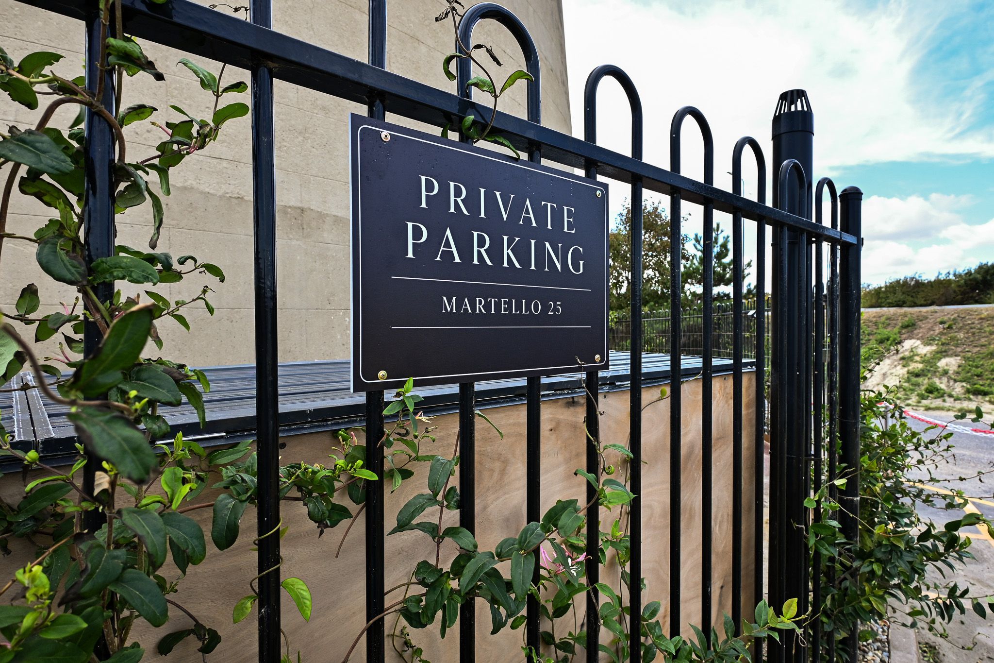 Placa de estacionamento privado com portão de metal e vegetação.