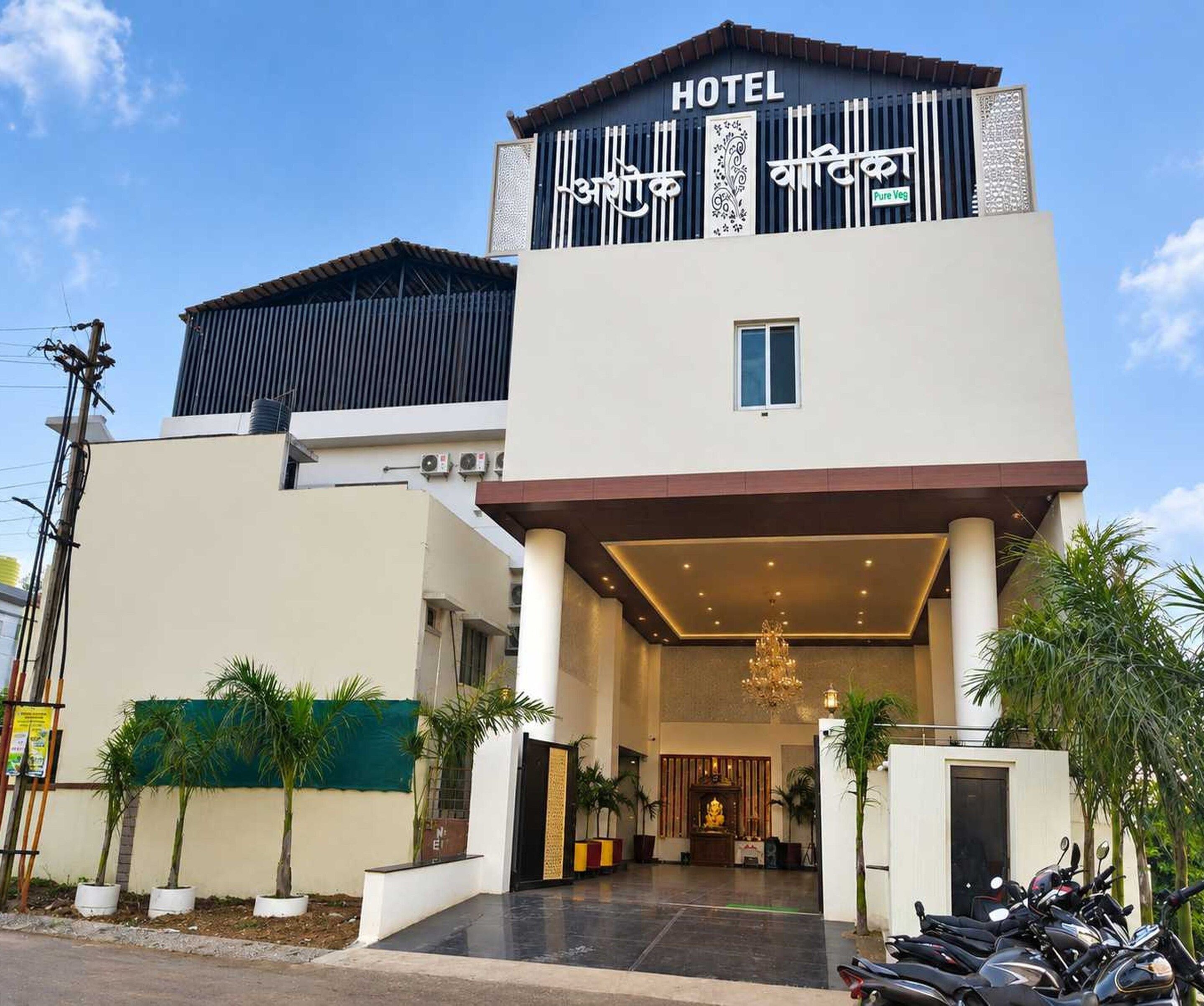 En hotelindgang med et overdækket område, en gylden statue og række af parkerede motorcykler.