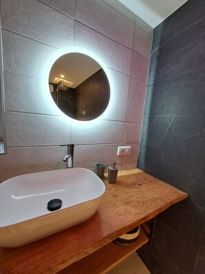 Une salle de bain avec un miroir rond, un lavabo blanc et un plan de toilette en bois.