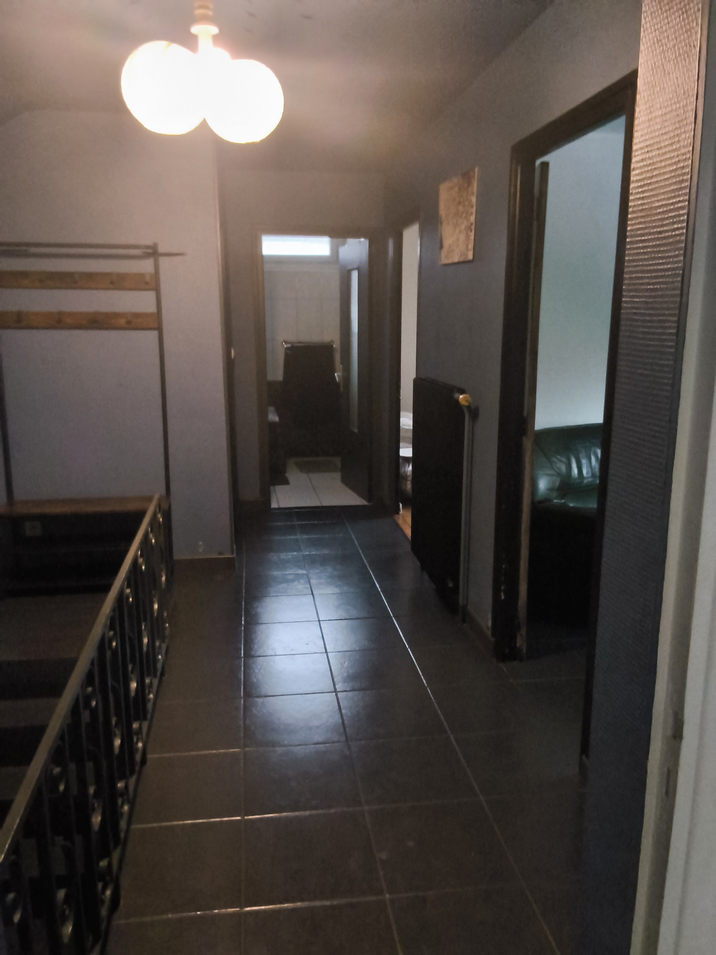 Un corridoio con pavimento piastrellato, una lampada a soffitto e una porta che dà su una stanza.