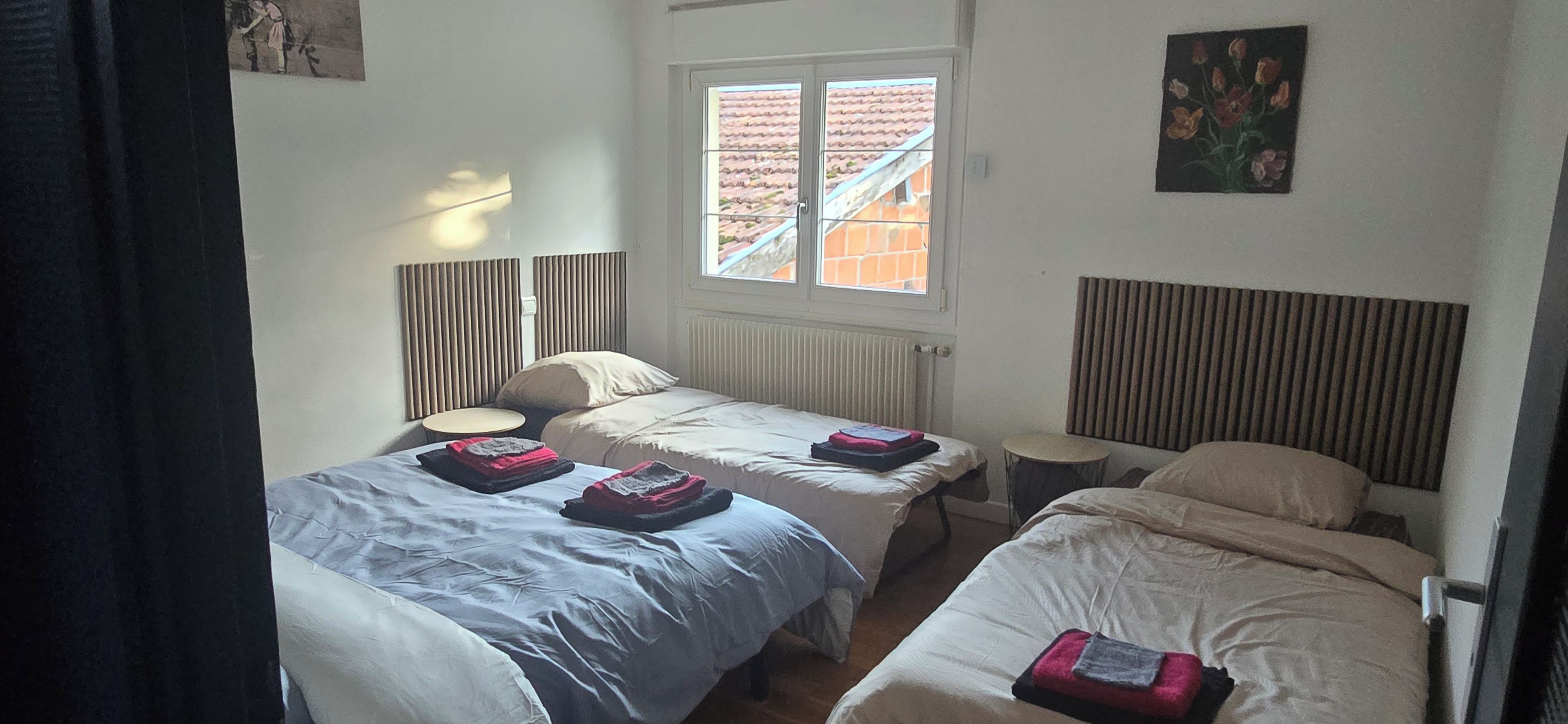 Een kamer met twee eenpersoonsbedden, een klein rond tafeltje, een radiator en een raam met uitzicht op gebouwen.