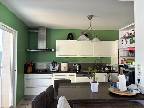 Une cuisine moderne avec des armoires blanches, une table à manger avec des chaises, un ventilateur de plafond et une plante en pot posée sur le comptoir.
