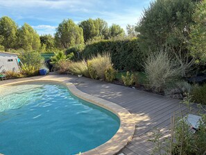 Une piscine dotée d’une terrasse en bois et entourée de verdure.
