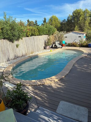 A swimming pool with a wooden deck, surrounded by a stone wall and various plants. - New Listing (34920 le cres)
