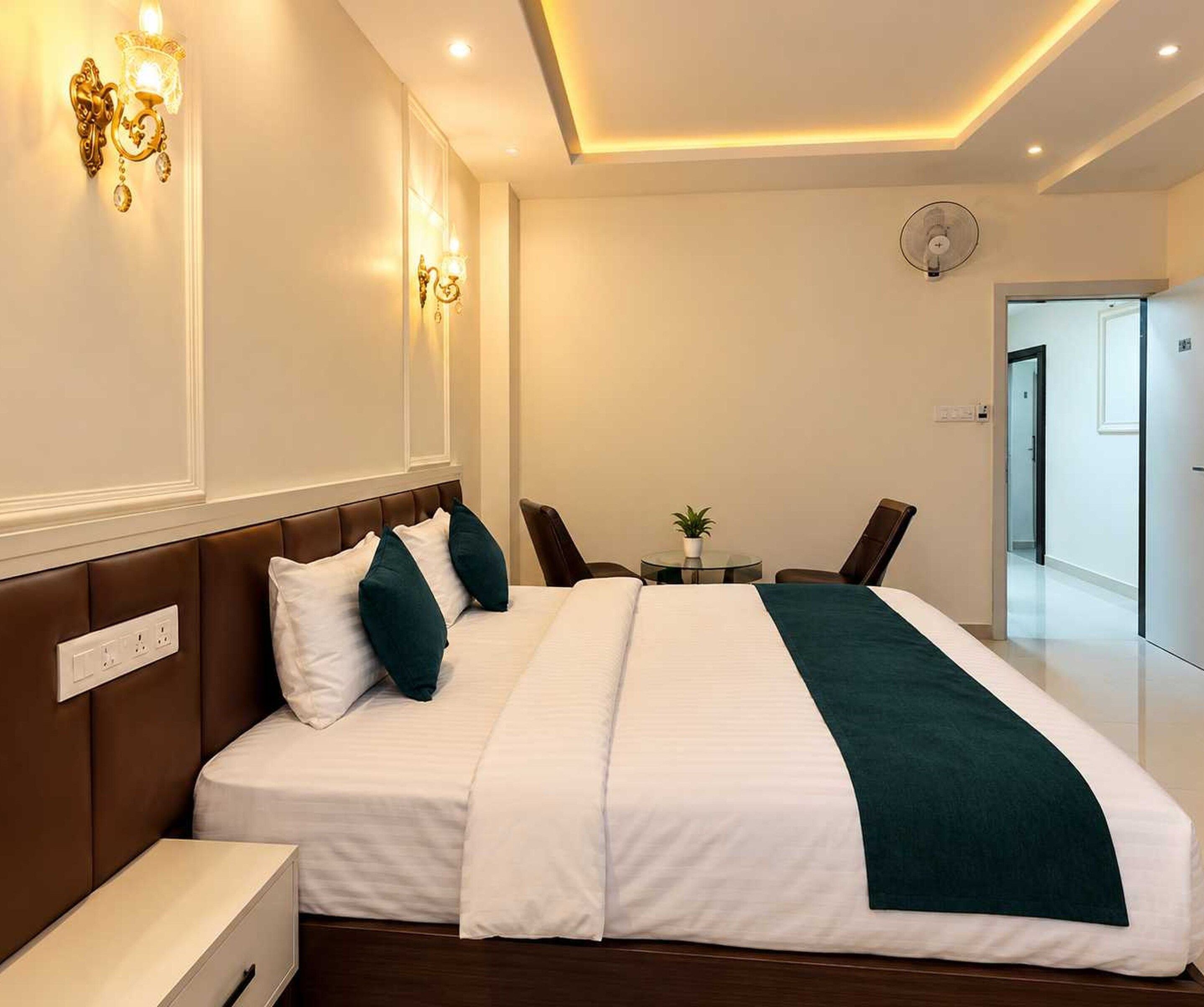 Une chambre d’hôtel comprenant un lit, une table de chevet, une lampe fixée au mur et une petite table avec des chaises.