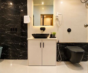 Een badkamer met een zwarte marmeren wand, een witte wastafel met een zwart bassin, een spiegel, een wit toilet en een douchehoek.
