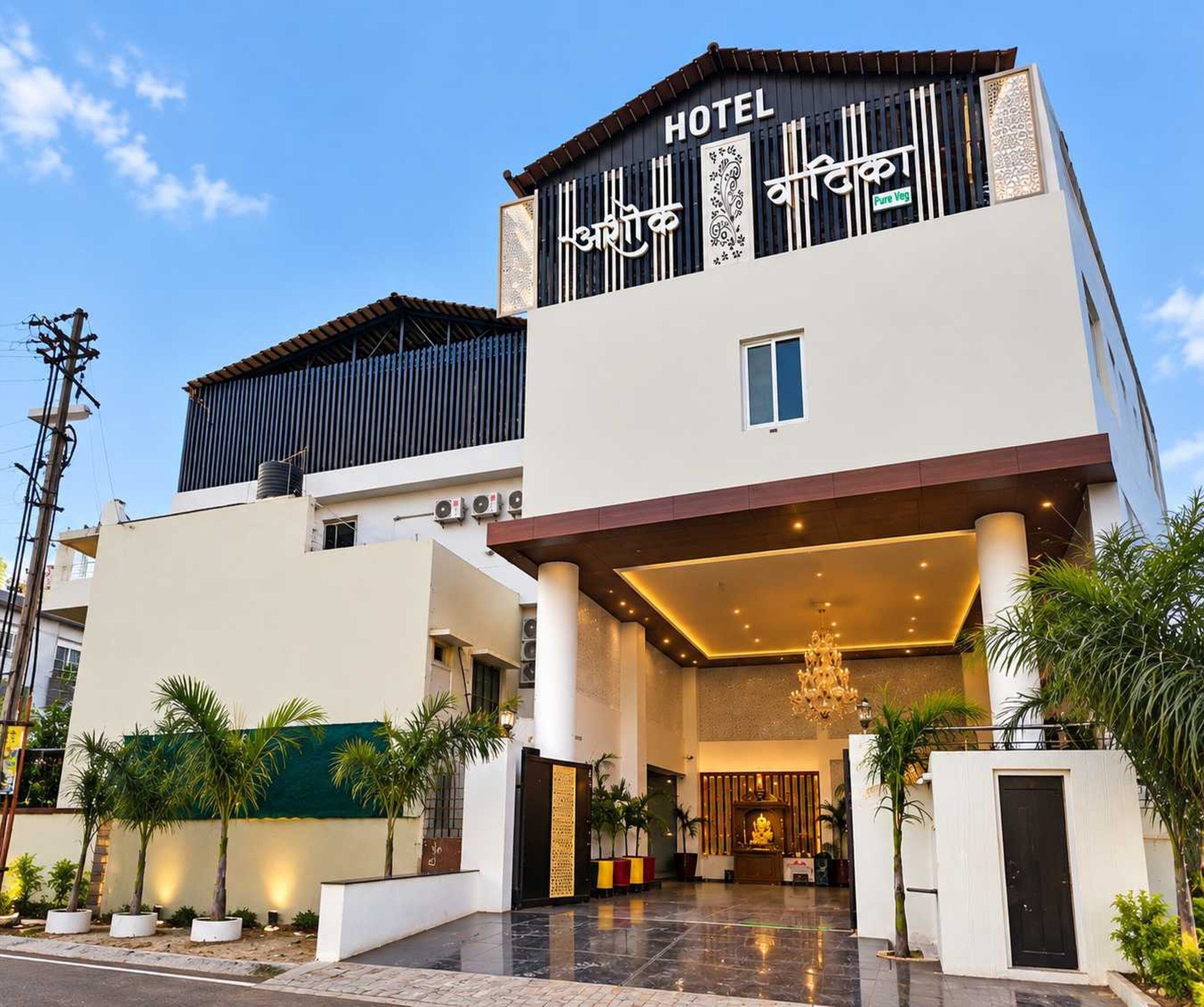 Een hotel met een moderne gevel, een opvallende ingang met een kroonluchter en een bordje dat vegetarische opties aangeeft.