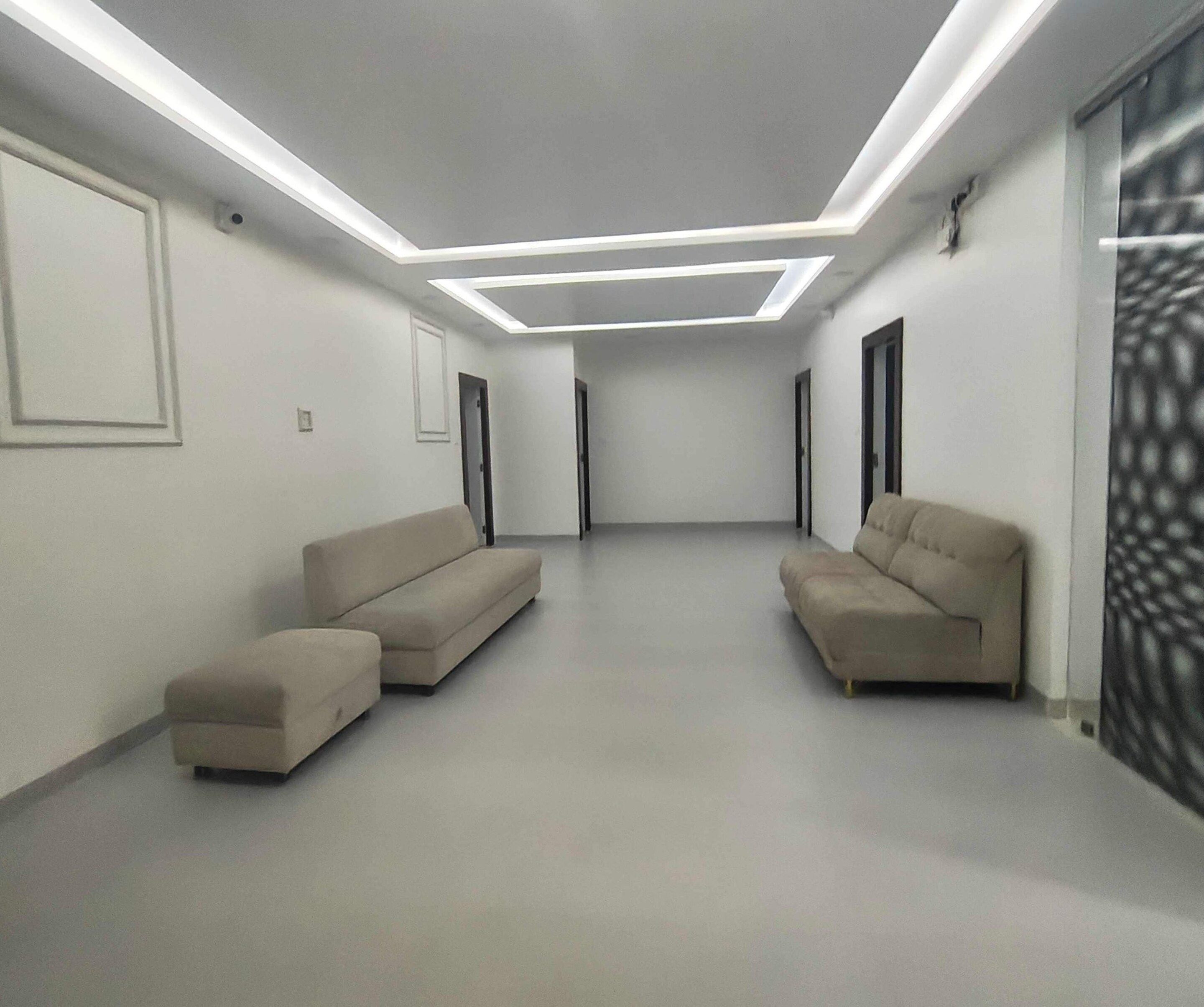 Un intérieur moderne avec deux canapés et un petit pouf, un plafond doté d’un éclairage encastré et un mur à motifs sur la droite.
