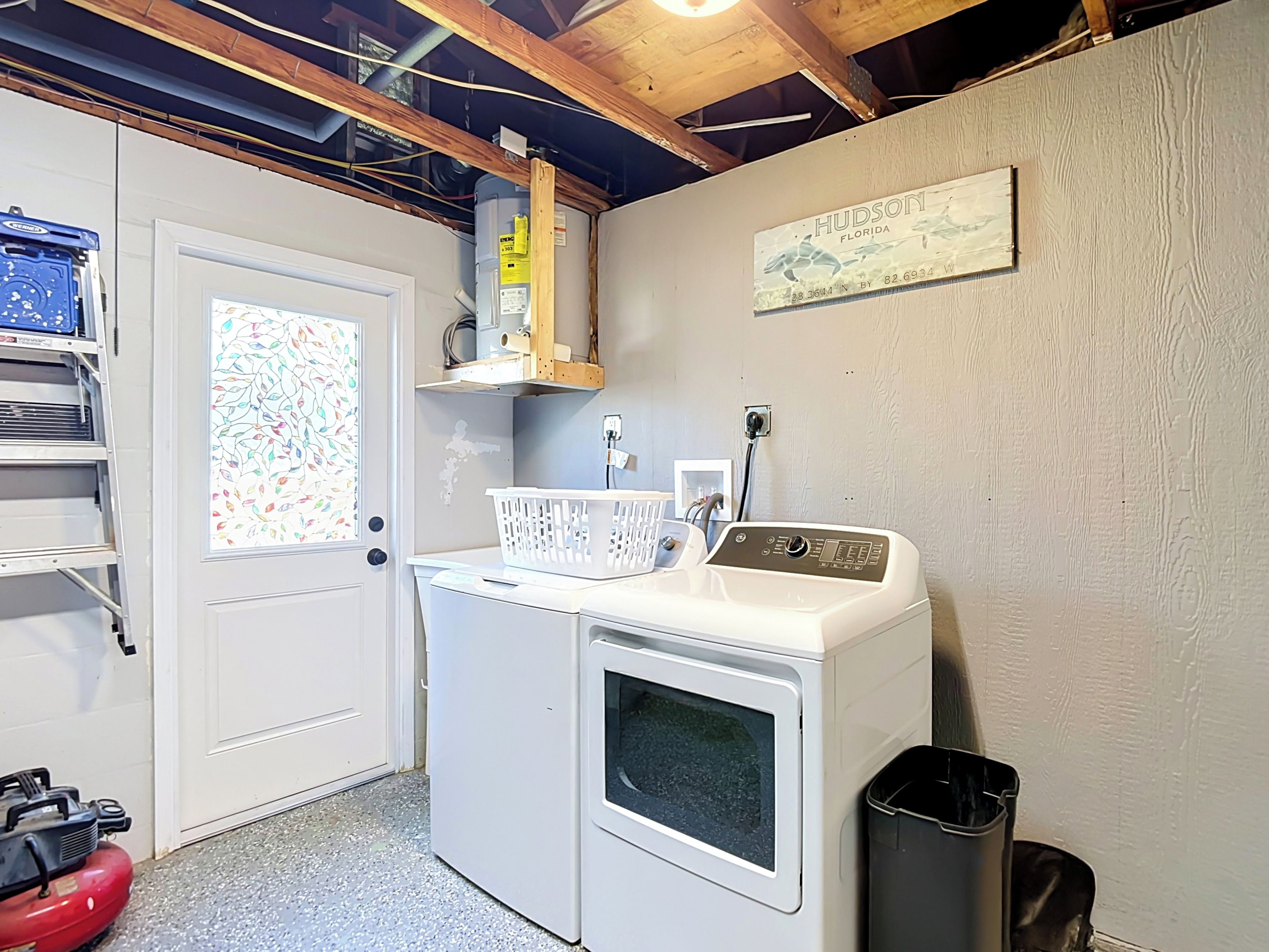 A laundry room with a washing machine, a dryer, a water heater, and a wall-mounted sign.