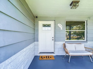 A front porch with a white door, a wicker chair, a 'hello' mat, and a mailbox. - Waterfront 2-bedroom house with direct access to the Gulf in Hudson, Fl. (Hudson)