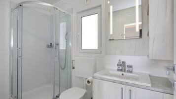 Un baño moderno con ducha envuelta en vidrio, inodoro y lavabo con espejo arriba.