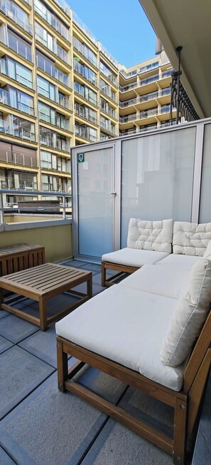Ein Balkon mit einer Couch und einem Tisch, mit Blick auf ein Hochhaus.