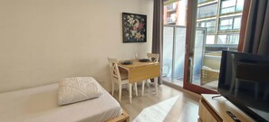 Una habitación pequeña con una cama, una mesa con sillas, un cuadro en la pared y un televisor.