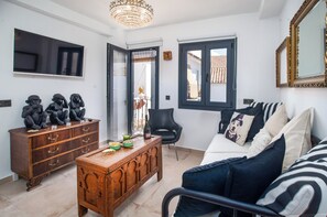 Un salon comprenant un canapé, une table basse en bois, un téléviseur et un lustre.